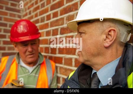 Workman et du site de construction foreman parle contre un mur arrière-plan. Banque D'Images