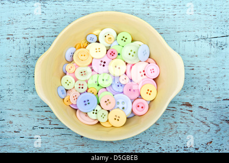 Les boutons de couleur pastel dans un bol jaune sur fond de bois vintage Banque D'Images