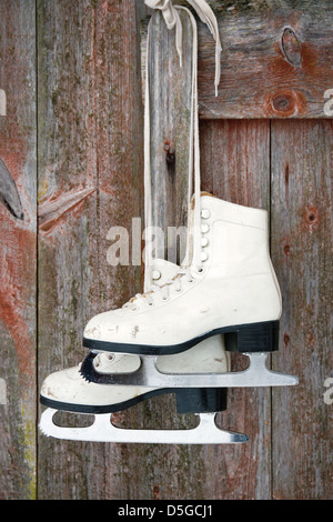 Ancienne figure des patins à glace accrochée à un mur rustique en bois rouge Banque D'Images