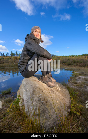 Jeune femme assise sur des rochers près d'un étang. Banque D'Images