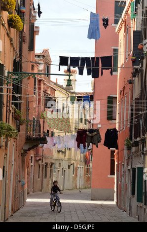 Garçon sur sa bicyclette dans la rue ci-dessous blanchisserie séchage à Venise, Italie. Banque D'Images