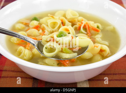 Une assiette de soupe au bouillon de poulet avec des pâtes et des légumes dans un bol blanc sur une nappe colorée. Banque D'Images