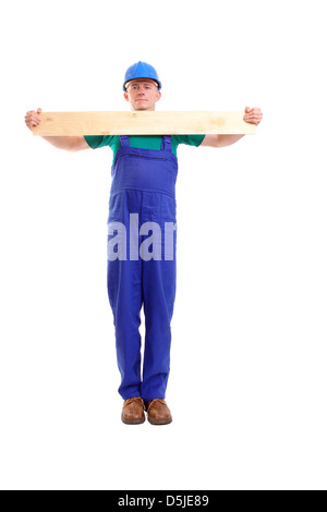 Builder wearing blue jumpsuit et helmet holding planche en bois en face de lui - sur fond blanc Banque D'Images