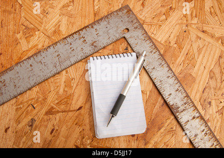 L'ossature du charpentier square, le bloc-notes et un stylo sur le dessus de copeaux agglomérés - concept de planification de travail du bois Banque D'Images