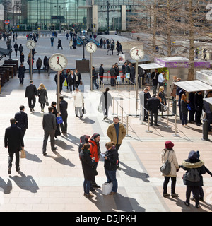 Employés de bureau à l'heure du déjeuner sur Canary Wharf plaza avec groupe d'horloges sur les poteaux à Londres Docklands Isle of Dogs Tower Hamlets est de Londres Angleterre Royaume-Uni Banque D'Images