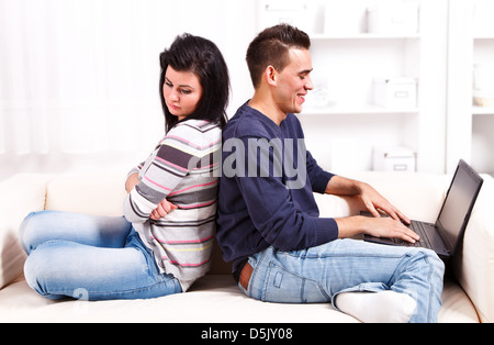 Jeune couple assis dos à dos sur le canapé, l'homme jouissant de la femme, de l'ordinateur est triste et se sentir négligés Banque D'Images