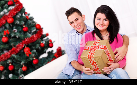 Smiling young couple sitting on sofa blanc avec un don near Christmas Tree Banque D'Images