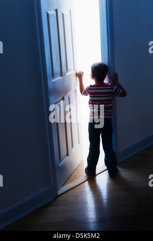 Boy (4-5) peeking through doorway Banque D'Images