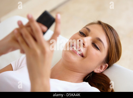 Young woman lying on bed and using cell phone Banque D'Images