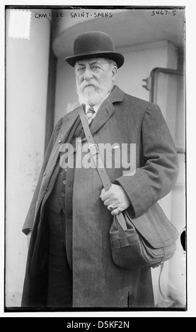 Cette photographie représente Camille Saint-Saëns, célèbre compositeur français, prise en 1915. L'image le capture debout près d'une sacoche, mettant en valeur son apparence distinguée. Banque D'Images