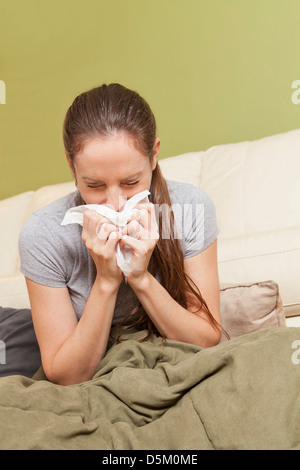 Woman blowing her nose sur canapé Banque D'Images