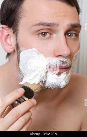 Jeune homme s'appliquer la crème à raser sur le visage Banque D'Images