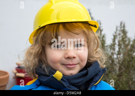 3 ans garçon joue à la maison. L'assemblage à toy house, porte un casque de jouet. Ressemble à un architecte. Banque D'Images