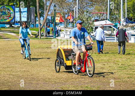 Les parents sur les cycles avec leur enfant sur remorque derrière le père dans une remorque couverte en Marina Jack Park Sarasota Banque D'Images