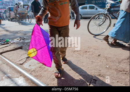 Un garçon marche à travers un street dans le soleil avec un cerf-volant de papier de couleur vive. Varanasi, Inde. Banque D'Images