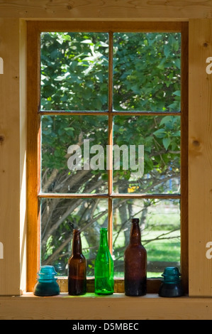 Une vieille ferme appui de fenêtre est titulaire de bouteilles et de verre ancien isolateurs télégraphiques qui capturent la lumière du matin. Banque D'Images