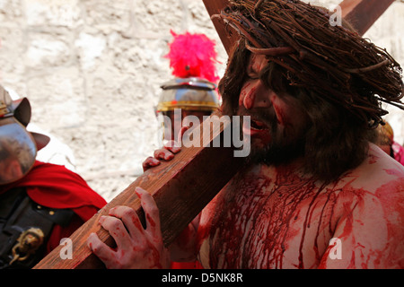 Un chrétien dévot habillé en Jésus Christ porte une croix en bois reproduisant le Chemin de Croix du Vendredi saint au cours de procession le long de la Via Dolorosa street que l'on croit être le chemin que Jésus a marché sur le chemin de sa crucifixion dans la vieille ville de Jérusalem-Est, Israël Banque D'Images