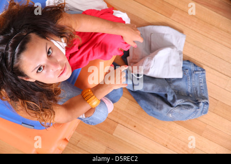 Une jeune femme assise sur une pile de valises avec trop de vêtements pour s'intégrer. Banque D'Images