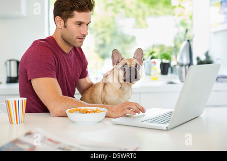 Man on laptop petting dog in kitchen Banque D'Images