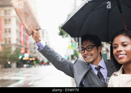 Business people hailing taxi on city street Banque D'Images