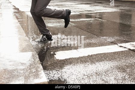 Businessman stepping in puddle on city street Banque D'Images