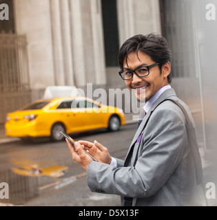 Businessman using cell phone on city street Banque D'Images