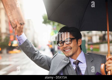 Businessman hailing taxi on city street Banque D'Images