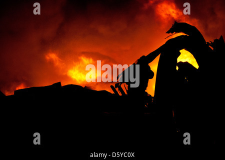 Silhouette de pompiers la lutte contre un feu faisant rage avec d'immenses flammes de bois brûlant Banque D'Images