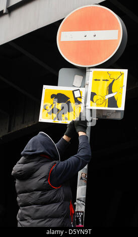 Artiste El Bocho démontre comment il attache un de ses pictogrammes pour un poteau de signalisation à Berlin, Allemagne, 31 octobre 2012. La photo présente une scène où quelqu'un est battu pendant que quelqu'un filme la scène avec un téléphone mobile. Strett El Bocho artiste de Berlin a commencé un art d'action contre la violence dans les grandes villes, le 31 octobre 2012. Il a l'intention de mettre en place plus de 250 pictogrammes Banque D'Images