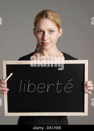 Portrait of young businesswoman holding tableau noir avec texte français 'liberté' (liberté) Banque D'Images