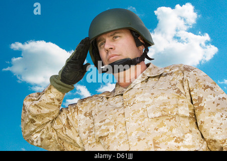 Mid-adult soldat en uniforme militaire saluant contre ciel nuageux Banque D'Images