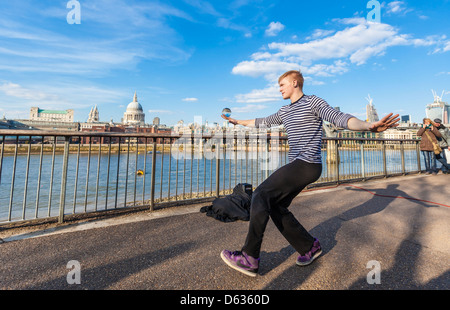 Un artiste de rue qui jongle avec une boule de cristal sur la promenade de la Tamise, South Bank, Londres, Angleterre, Royaume-Uni. Banque D'Images