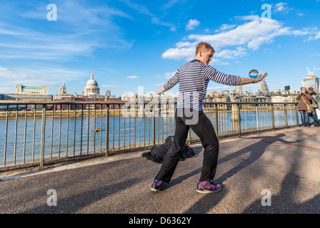 Un artiste de la rue qui jongle avec une orbe de cristal sur la promenade de la Tamise, South Bank, Londres, Angleterre, Royaume-Uni. Banque D'Images