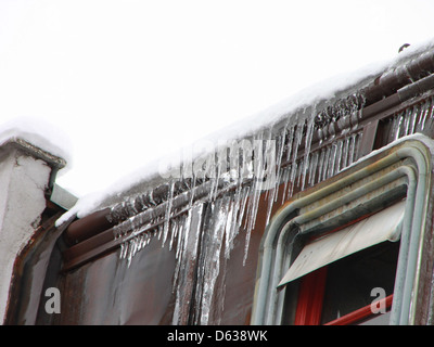 Cette image montre des glaçons suspendus au bord d'un toit, formés par l'eau gelée par temps froid. La photo souligne la structure délicate et nette des formations de glace. Banque D'Images