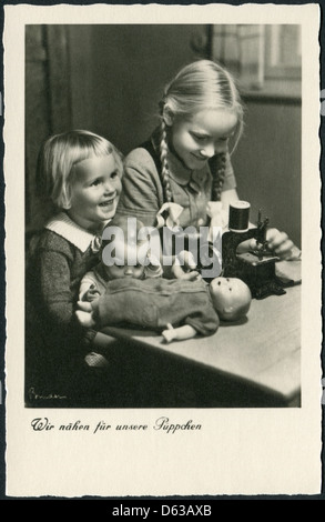 Ancienne carte postale allemande, vers 1938. Les filles jouent dans les égouts. Inscription en allemand : Nous avons cousu pour nos poupées. Banque D'Images