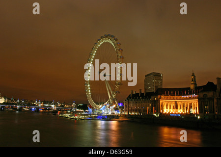 Le London Eye éclairés la nuit prochaine à County Hall, près de la Tamise. Banque D'Images