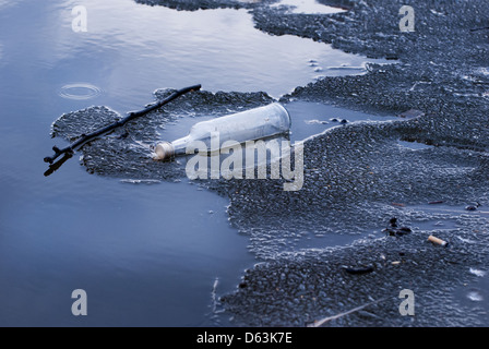 Le flacon en verre des ordures sur la fonte des glaces sur le lac Banque D'Images