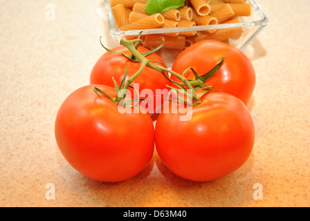 Quatre Tomates charnues devant un bol de pâtes de blé Banque D'Images