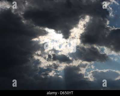 L'image montre des rayons lumineux du soleil perçant à travers les nuages sombres pendant une journée d'été. L'effet de lumière spectaculaire capture le contraste puissant entre la lumière et l'ombre dans le ciel. Banque D'Images
