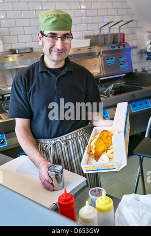 Un homme qui sert du poisson et des frites dans un poisson traditionnel britannique et chip shop Banque D'Images
