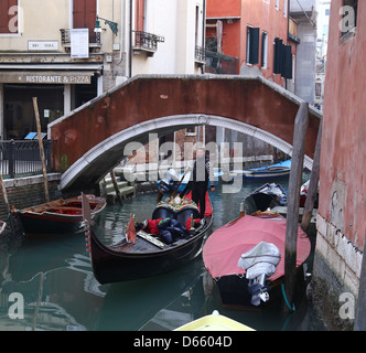 Un gondolier et sa gondole sur un petit canal latéral avec des vieux bâtiments et des bateaux, et un pont à Venise Italie Banque D'Images