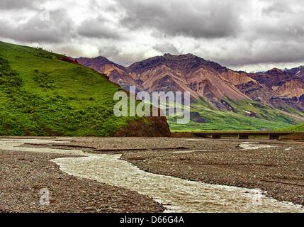 27 juin 2012 - L'Arrondissement de Denali, Alaska, États-Unis - nuages de tempête de recueillir plus de la vallée glaciaire de sculpté à la Toklat, l'un de la tresse de rivières à travers la forêt boréale et de la toundra du 6 million d'acres (24,500åÊkm) Parc National Denali et préserver. Chargé avec des débris de roche glaciaire et le ruissellement de la neige fondante, elles évoluent et s'entremêlent leurs chaînes sur la vallée et d' influence radicalement la topographie. Robuste, Multi-couleur de la montagnes polychromes de l'Alaska augmentation de la distance au-delà de l'Toklat River Bridge. (Crédit Image : © Arnold Drapkin/ZUMAPRESS.com) Banque D'Images