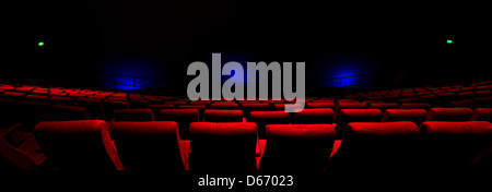 Des rangées de fauteuils rouges dans une salle obscure avec feux bleus brillant sur l'écran. Banque D'Images