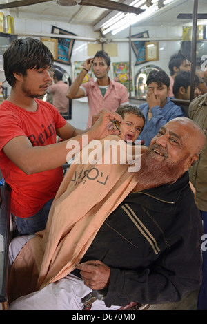 Un salon de coiffure donne une petite fille du père une coupe de cheveux dans une locaux de fortune dans un bidonville de vieux Delhi en Inde Banque D'Images