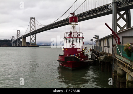 Un bateau-pompe amarré à une jetée dans la baie de San Francisco avec une vue sur le Bay Bridge et l'île de Yerba Buena vu de Fort Mason. Banque D'Images