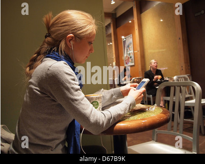 Jeune femme la lecture de messages texte sur son iPhone dans un café à New York, NY, le 11 avril 2013, © Katharine Andriotis Banque D'Images