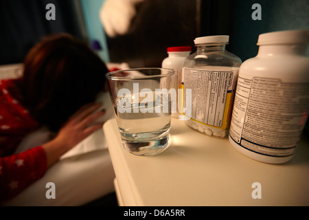 Verre d'eau et des bouteilles de pilules sur la table de chevet de la jeune vingtaine femme se réveiller dans le lit dans une chambre à coucher Banque D'Images