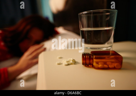 Verre d'eau et de bouteilles de somnifères sur la table de chevet de la jeune vingtaine, femme au lit dans une chambre à coucher Banque D'Images