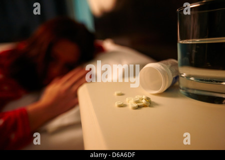 Verre d'eau et de bouteilles de somnifères sur la table de chevet de la jeune vingtaine, femme au lit dans une chambre à coucher Banque D'Images