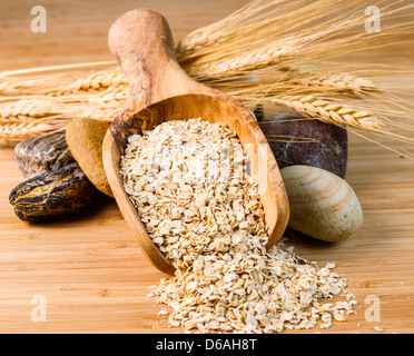 Photo horizontale d'avoine roulée en cuillère en bois avec des pierres rondes et les tiges de blé sur les produits de bois de bambou Banque D'Images